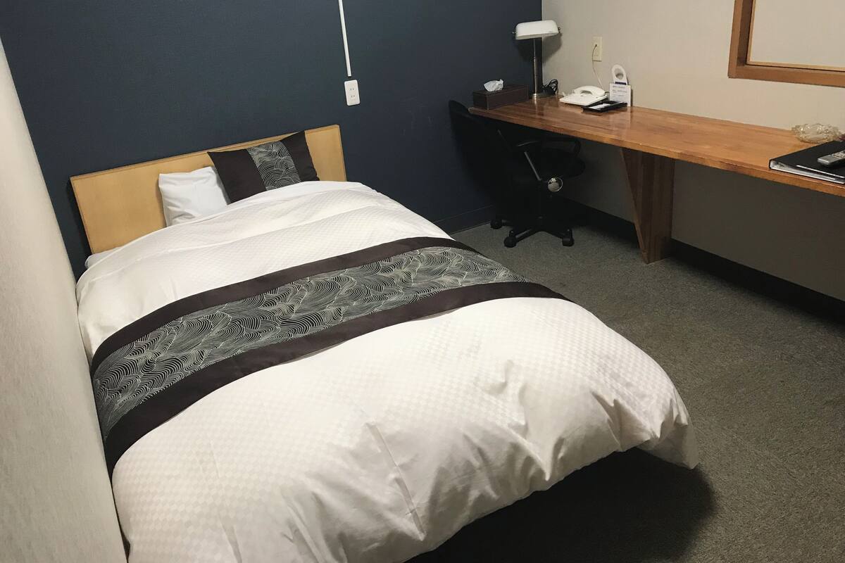 Ein Hotelzimmer mit Bett, Schreibtisch, Stuhl, Lampe und Telefon.