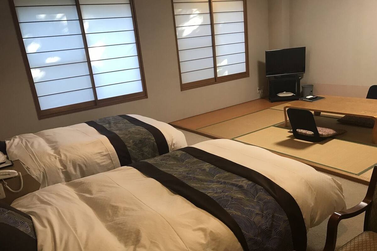 Ein Hotelzimmer mit zwei Betten, einem Fernseher, einem Schreibtisch und einem Stuhl.