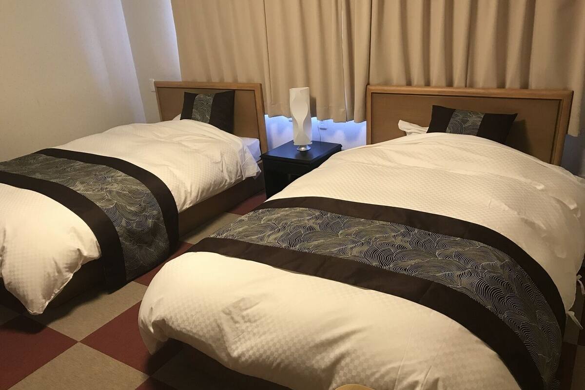Ein Hotelzimmer mit zwei Betten, jeweils mit Kopfteil, Nachttisch und Lampe.