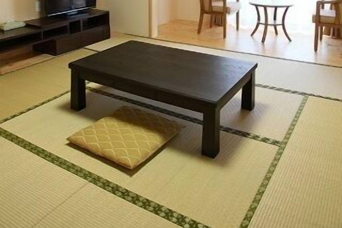 Ein Wohnzimmer mit Fernseher, einem dunklen Holztisch, Tatami-Matten und einem Deckenventilator.