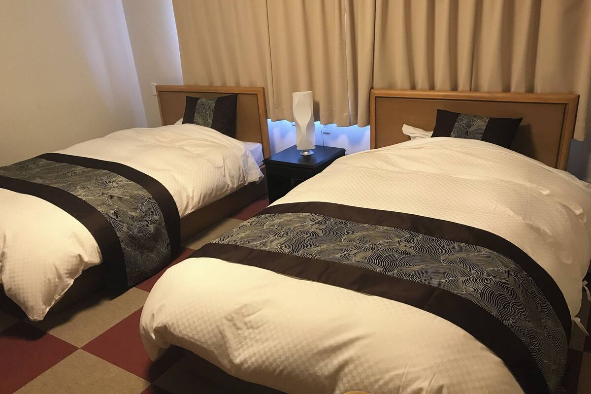 Zwei Betten mit je einem Einzelbett, ein Nachttisch mit Lampe und ein Schachbrettmuster-Boden.