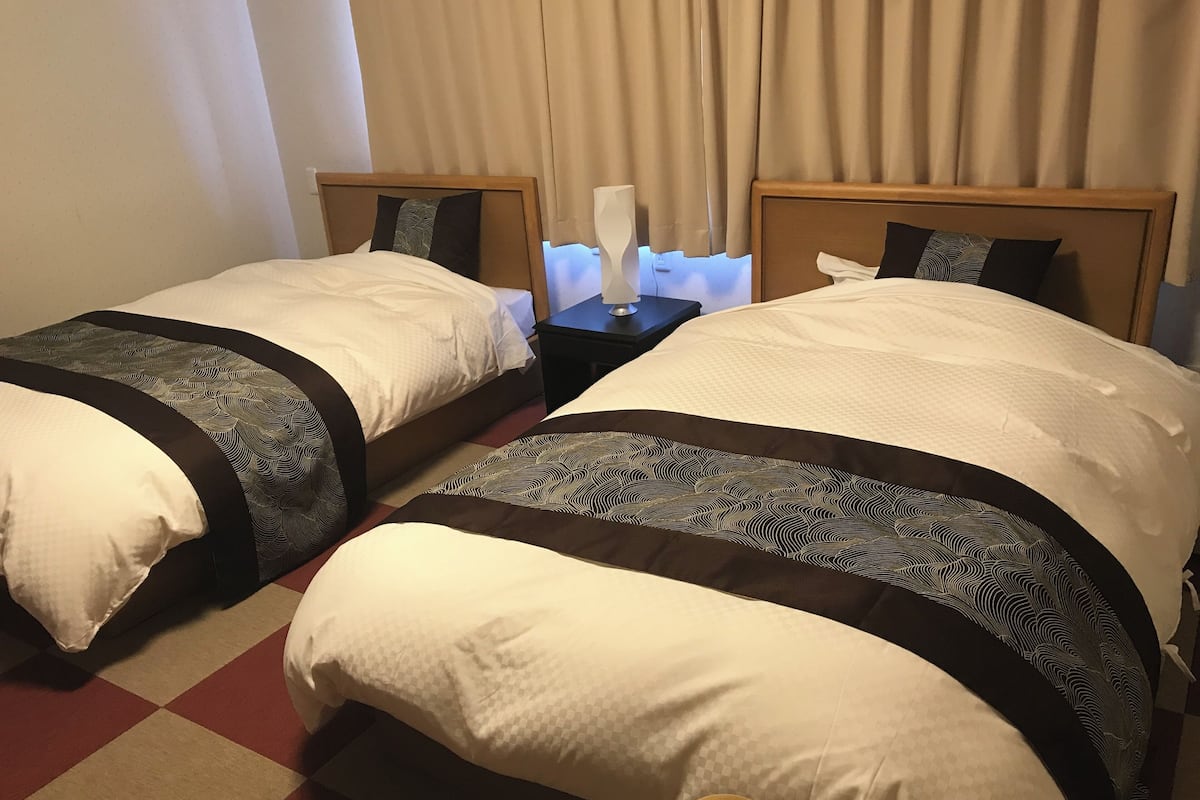 Dos camas individuales con ropa de cama estampada, una mesita de noche con lámpara y un suelo a cuadros.