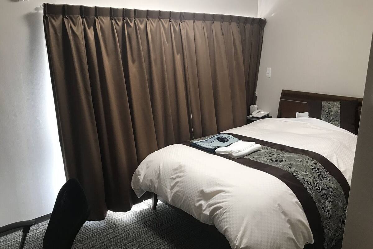 Ein Hotelzimmer mit Bett, Stuhl, Schreibtisch und Vorhang.
