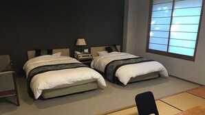 A hotel room with two beds, a bedside table with a lamp, a chair, and a tatami mat area. - Kyomachi Onsen Kyomachi Kanko Hotel (Ebino)