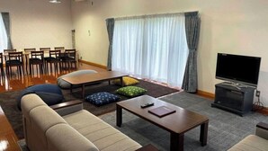 A living room with a sofa, coffee table, TV, and a dining area with chairs and a table. - Cottage Villa Top (Shintotsukawa)