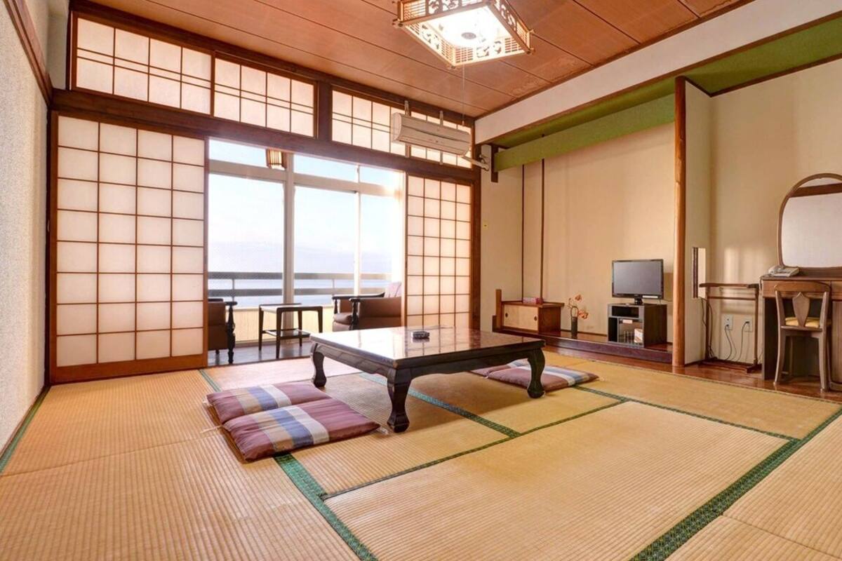 Ein traditioneller japanischer Raum mit Tatami-Böden, einem niedrigen Tisch, einem Fernseher und einem großen Spiegel.