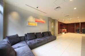 A modern hotel lobby with a grey sectional sofa, a reception desk, and a large wall art piece. - Richmond Hotel Nagoya Shinkansenguchi (Nagoya)