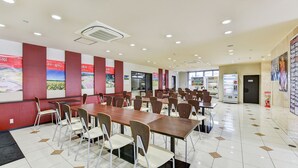 A spacious cafeteria with long tables and chairs, vending machines, and a fire extinguisher. - Hotel Primrose Saito (Saito)