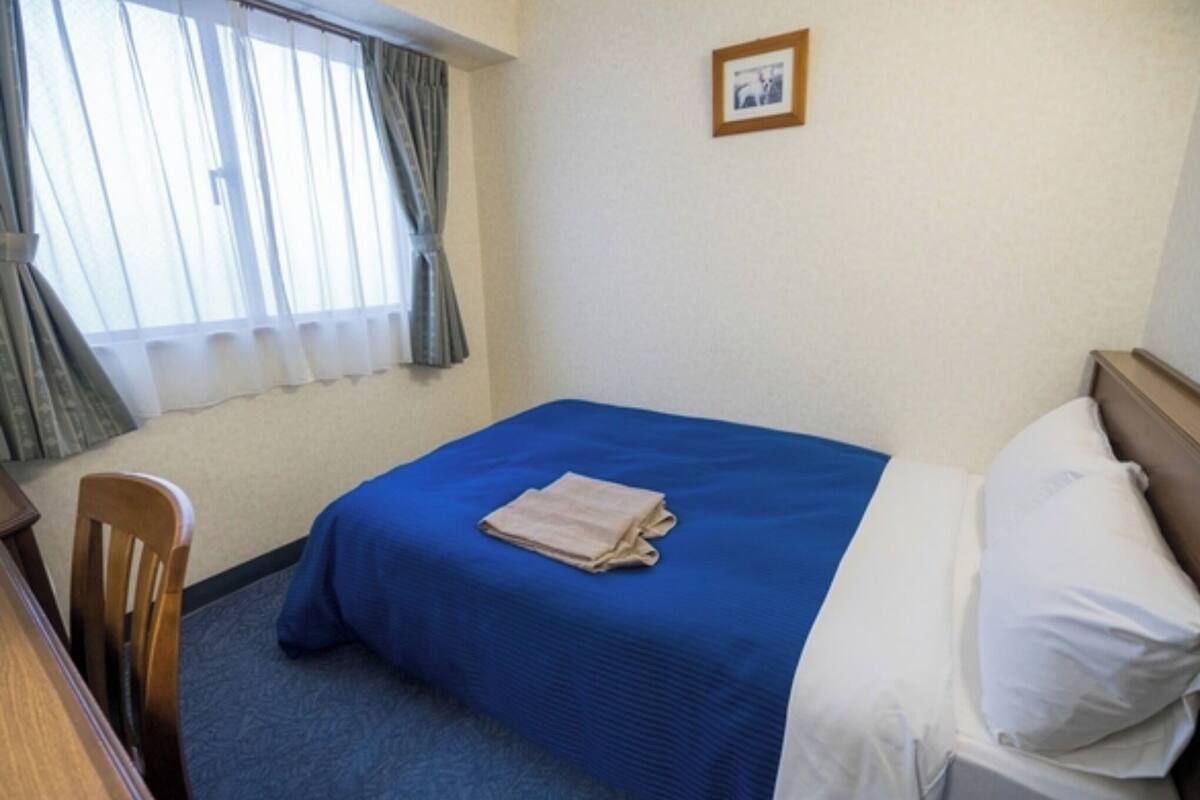 A hotel room with a single bed, a chair, a desk, and a window with curtains.