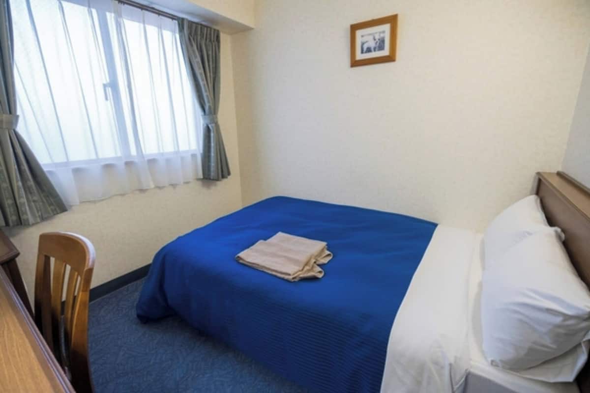 A hotel room with a single bed, a chair, a desk, and a window with curtains.