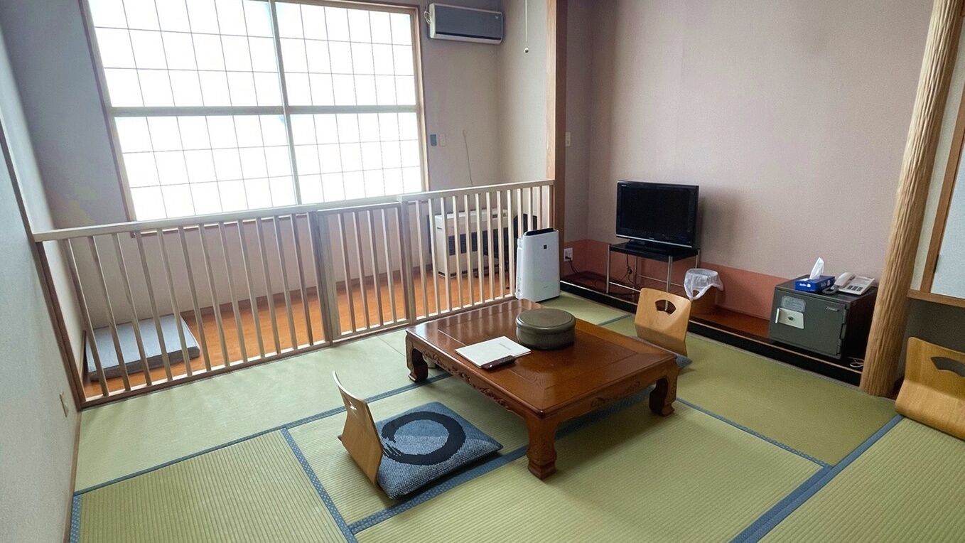 A room with tatami flooring, a wooden table, a television, and a futon bed.