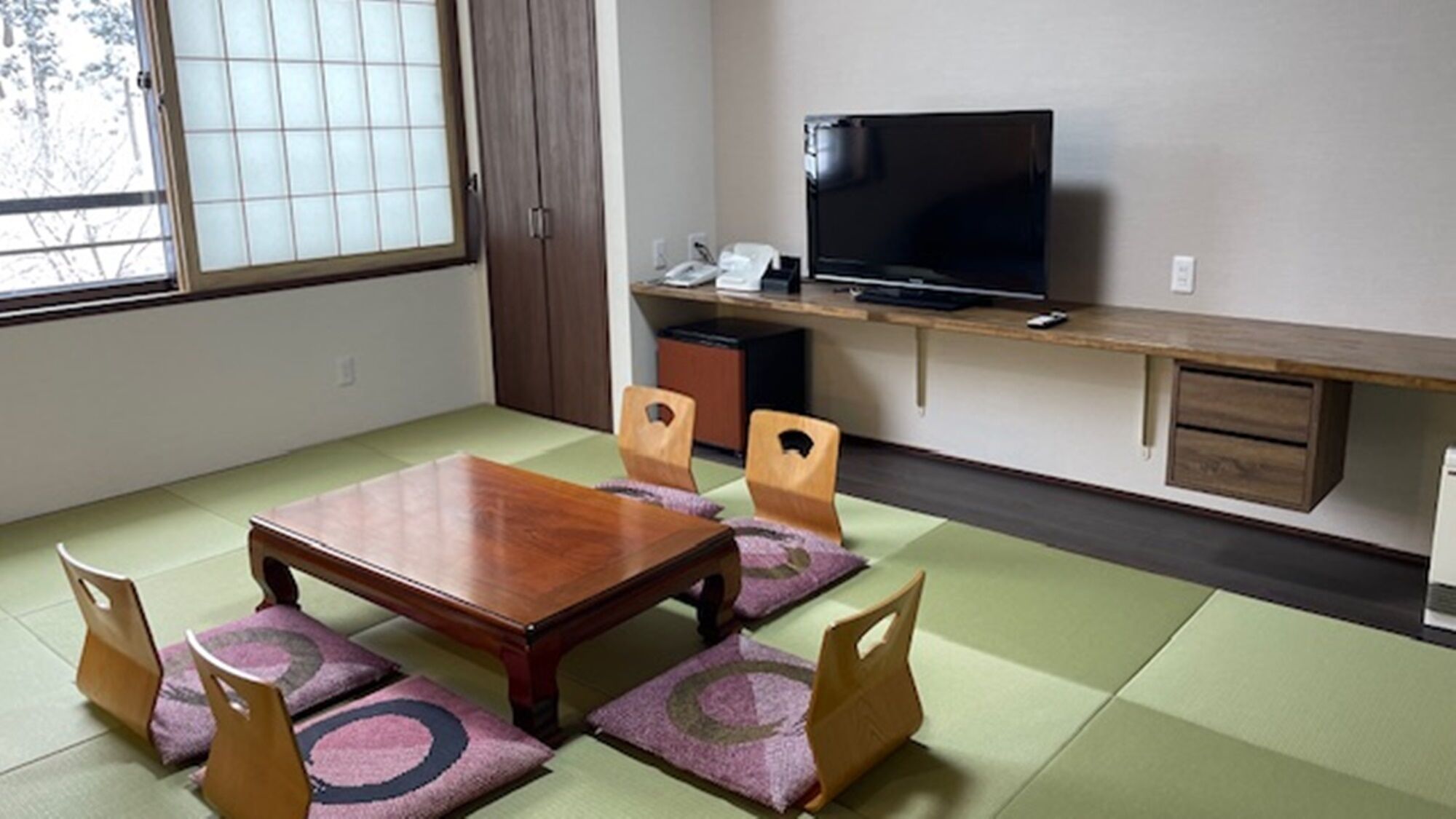 A traditional Japanese-style room with tatami flooring, a low wooden table, and a television on a wooden stand.