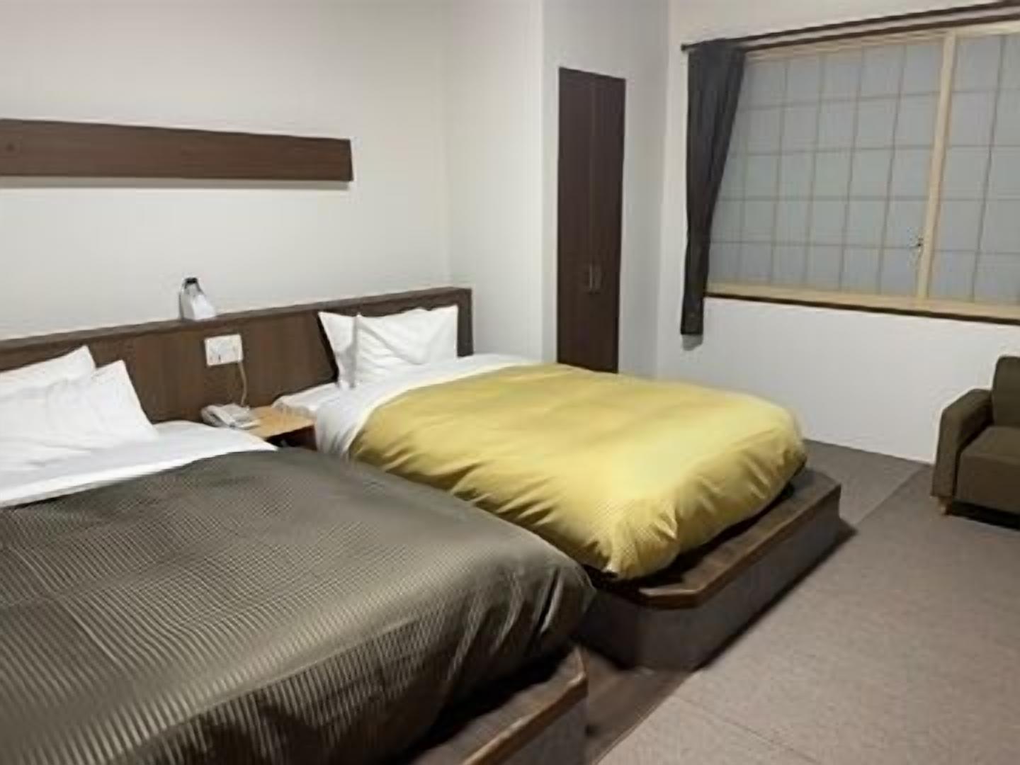 A hotel room with two beds, a nightstand, a desk, a chair, and a window with curtains.