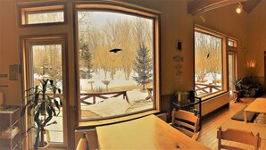 A cozy interior with a wooden staircase, large windows with views of trees, and a dining area with tables and chairs. - Forest Lodge Subaru (Teshikaga)