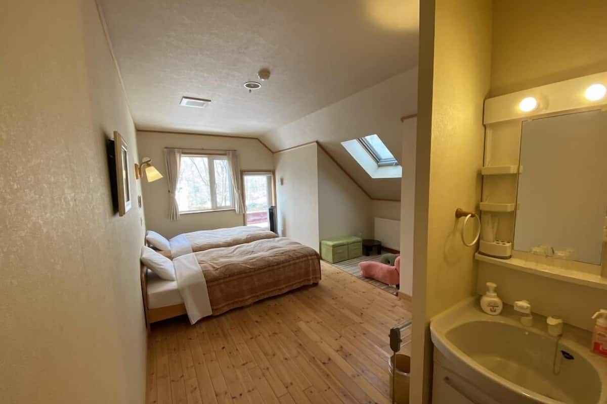 A bedroom with a bed, a skylight, a small green seating area, and a bathroom with a sink and mirror.