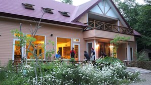 A building with a sloped roof, large windows, and a porch area. - Forest Lodge Subaru (Teshikaga)