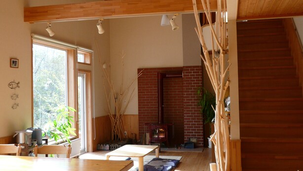 A spacious room with a high ceiling, wooden beams, a brick fireplace, and a staircase. - Forest Lodge Subaru (Teshikaga)