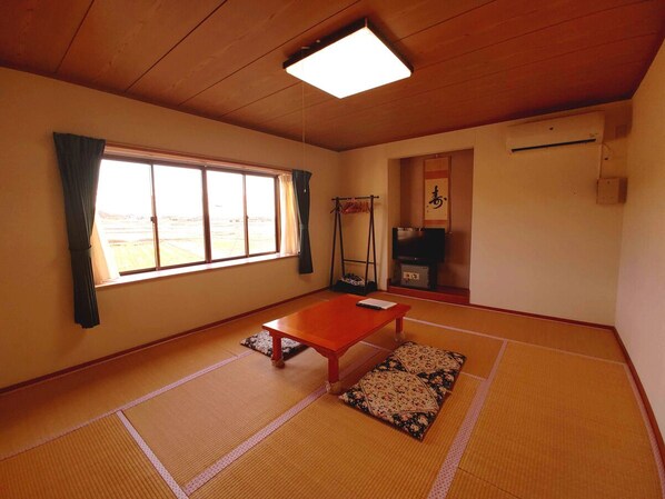 Una habitación con tatami, una mesa de madera, un futón, un televisor y una ventana con cortinas.