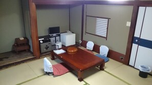 A traditional Japanese-style room with tatami flooring, a wooden table, and a TV on a cabinet.