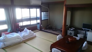A traditional Japanese room with tatami flooring, a futon bed, a shoji screen, a television, and a small shrine. - Komecho Ryokan (Imabari)