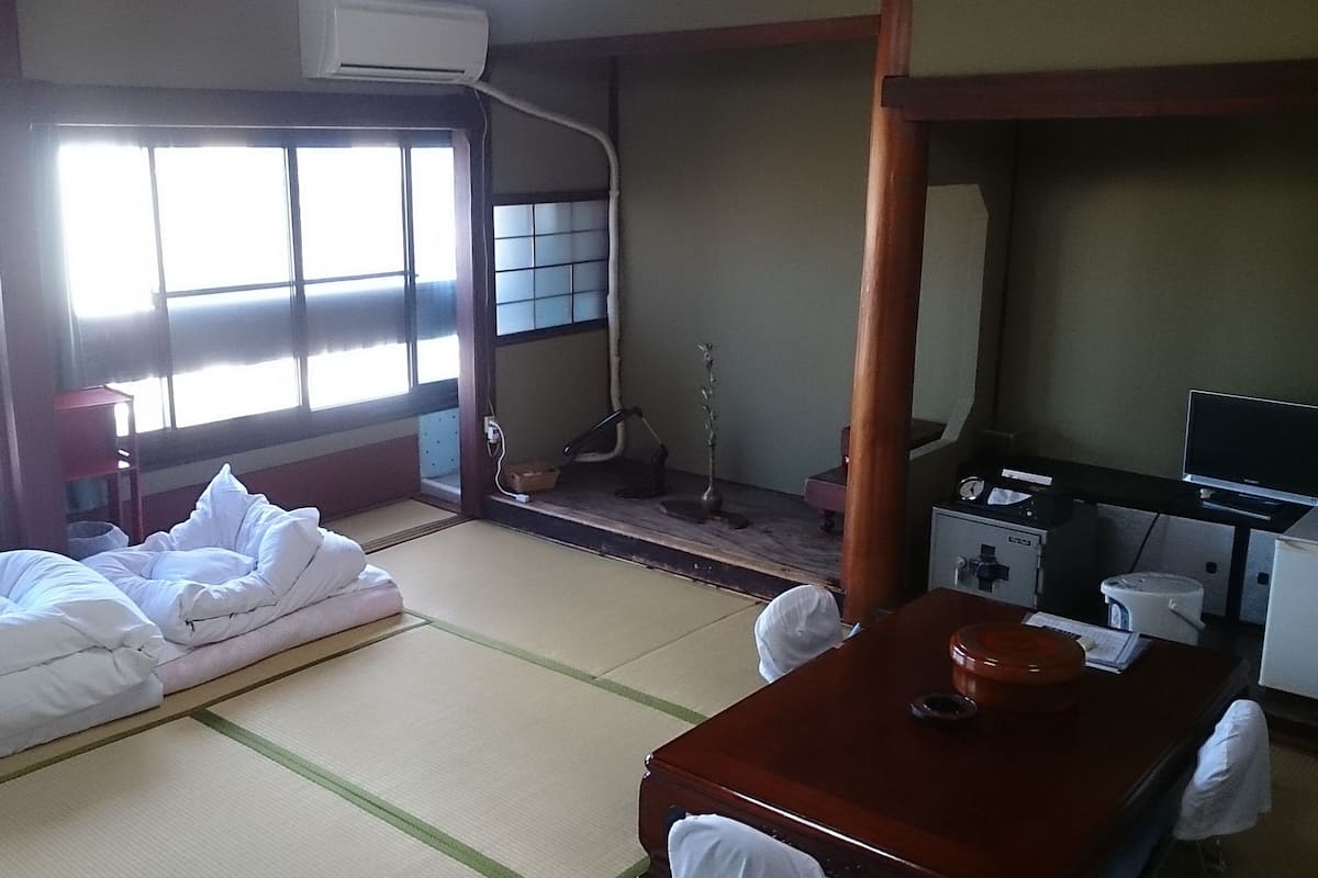 Una habitación japonesa tradicional con suelo de tatami, una cama futón, una pantalla shoji, un televisor y un pequeño santuario.