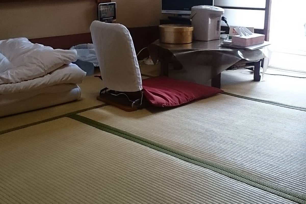 Una habitación tradicional japonesa con suelo de tatami, un futón, una mesita con televisor y una ventana con paneles shoji.