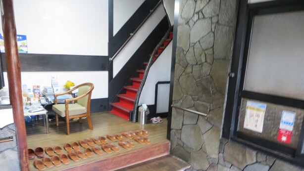 A staircase with a stone wall and a wooden platform holding shoes. - Komecho Ryokan (Imabari)
