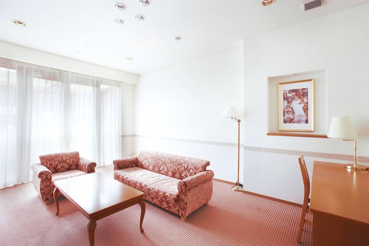 A hotel room with a sofa, a table, a chair, a lamp, and a framed picture on the wall.