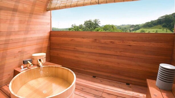 A wooden sauna with a large wooden tub, a wooden bench, and a stack of plates on a wooden deck.
