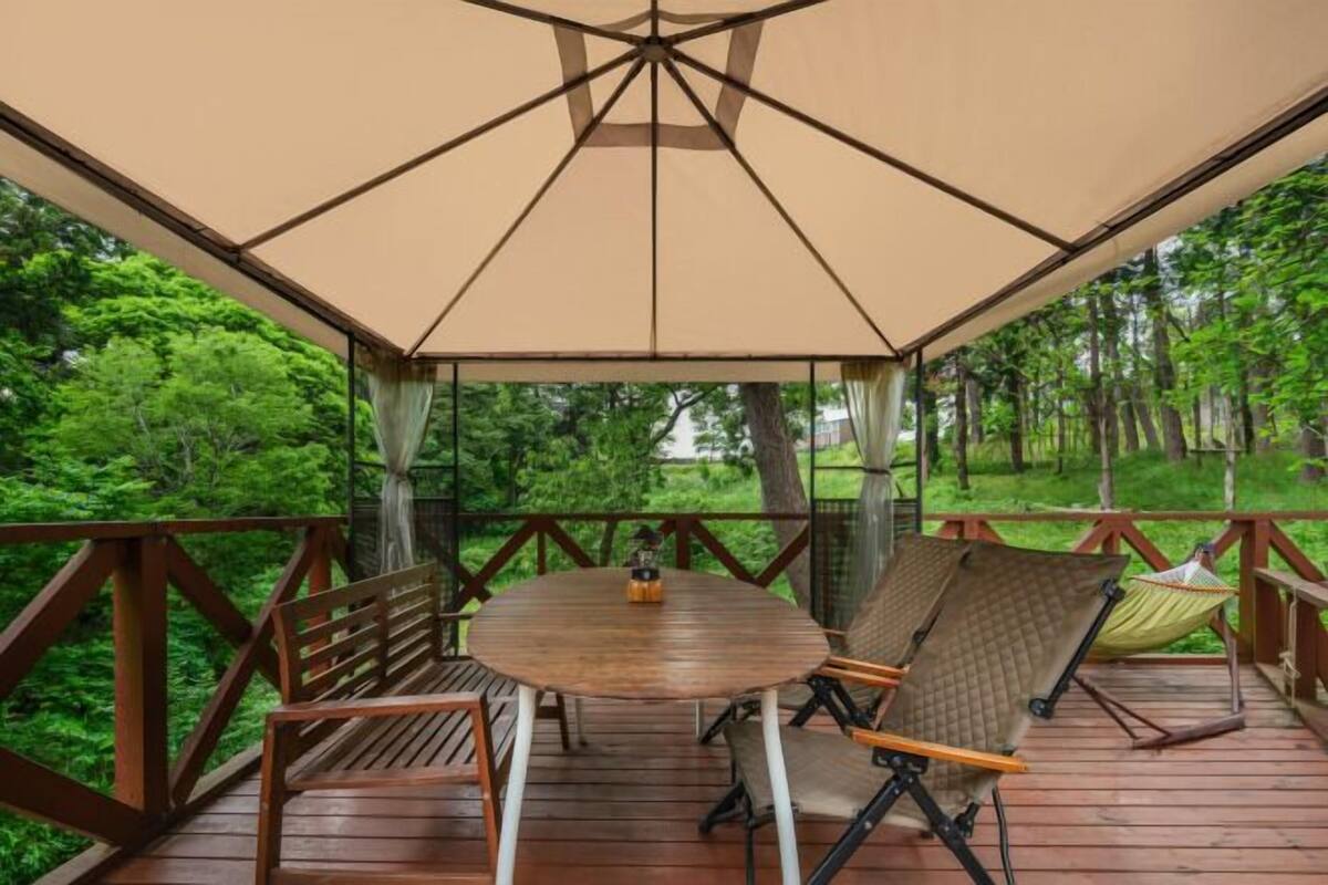 A wooden deck with a table and chairs, a hammock, and a canopy.