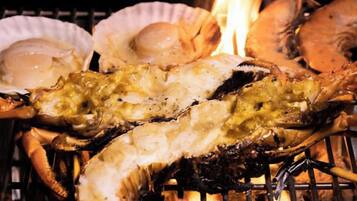 Grilled seafood, including lobster and clams, being cooked over an open flame.