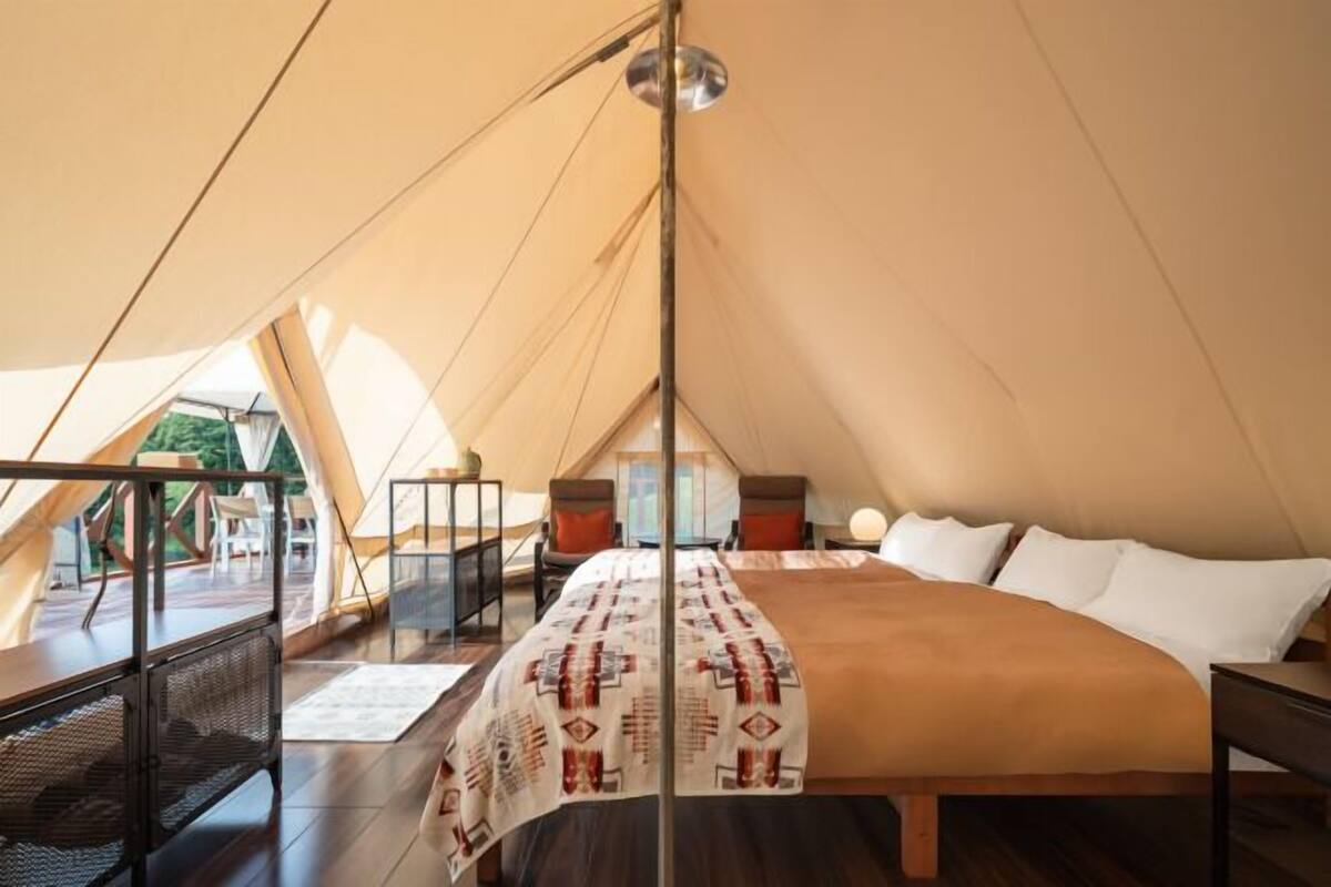 A cozy tented accommodation with a large bed, a desk, and a view of the outdoors.