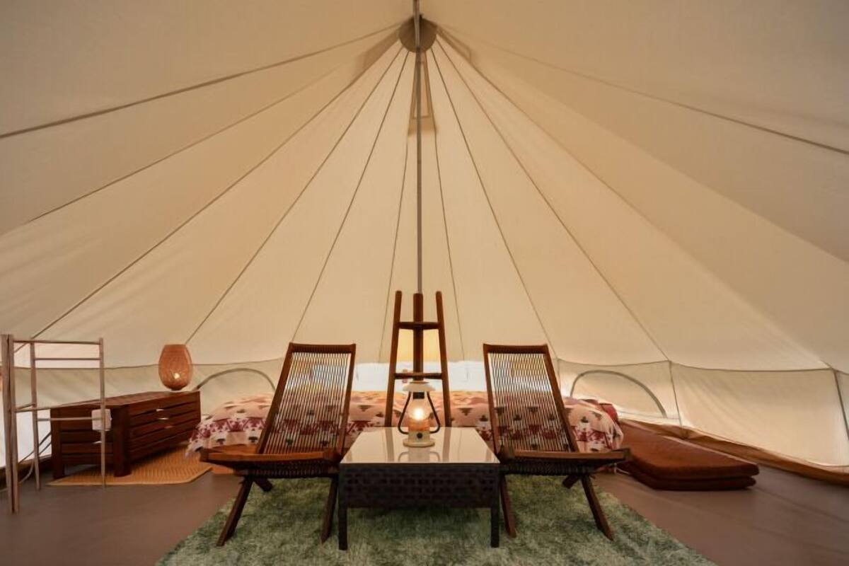 A tent with a central table, two chairs, a lamp, and a ladder.