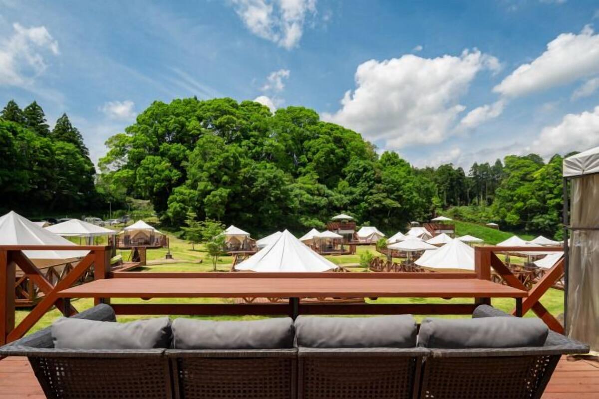 A wooden deck with wicker furniture and white tents in a forested area.