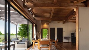 Un intérieur moderne avec un plafond en bois, un coin repas comprenant une table et des chaises, et de grandes fenêtres offrant une vue sur l’extérieur.