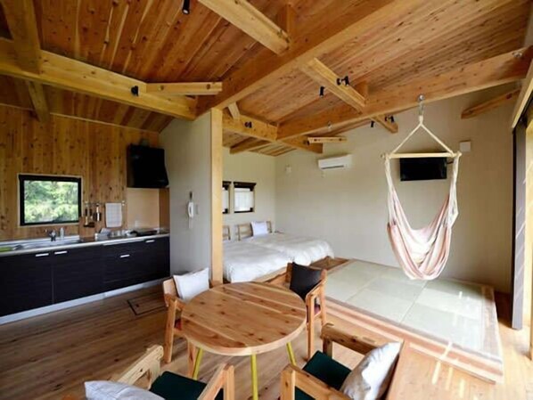 A wooden cabin interior with a kitchen, dining area, and a bed with a hanging hammock. - THE FARM Resort Japan (Katori-shi)
