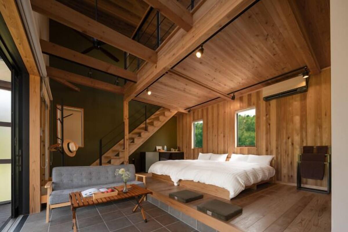 A modern bedroom with a large bed, a sofa, and a staircase.