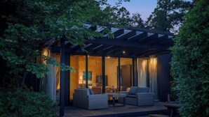 Un espace de vie extérieur moderne, doté d’une véranda en verre, d’une terrasse en bois et de mobilier d’extérieur.