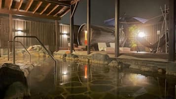 A hot spring area with a wooden deck, lounge chairs, and a stone pool.
