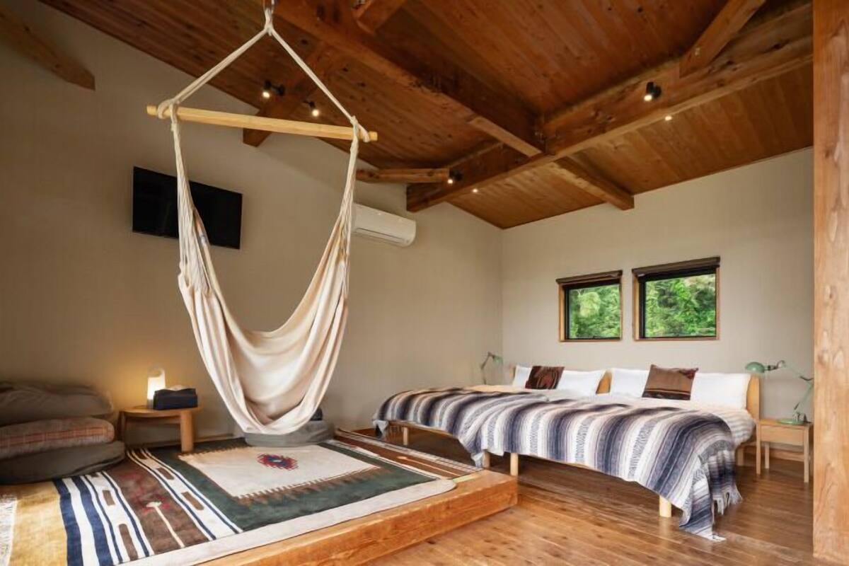 A bedroom with a canopy bed, a wooden ceiling, a large window, and a flat-screen TV.