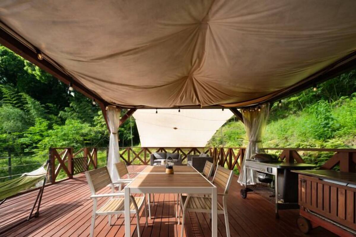 An outdoor deck with a table and chairs, a grill, and a canopy.