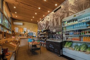 A store interior with wooden ceiling, shelves stocked with bottled beverages, and a refrigerated display with fresh produce. - THE FARM Resort Japan (Katori-shi)