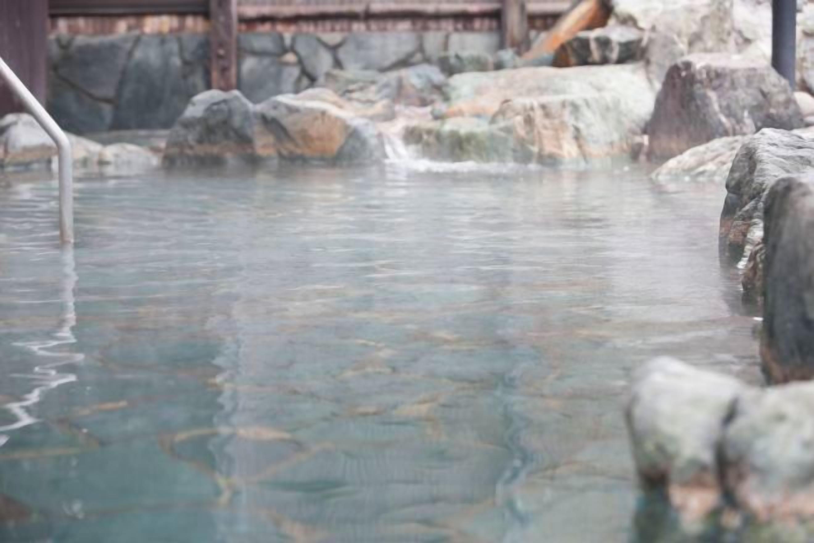 A clear pool with rocks and a wooden structure in the background.