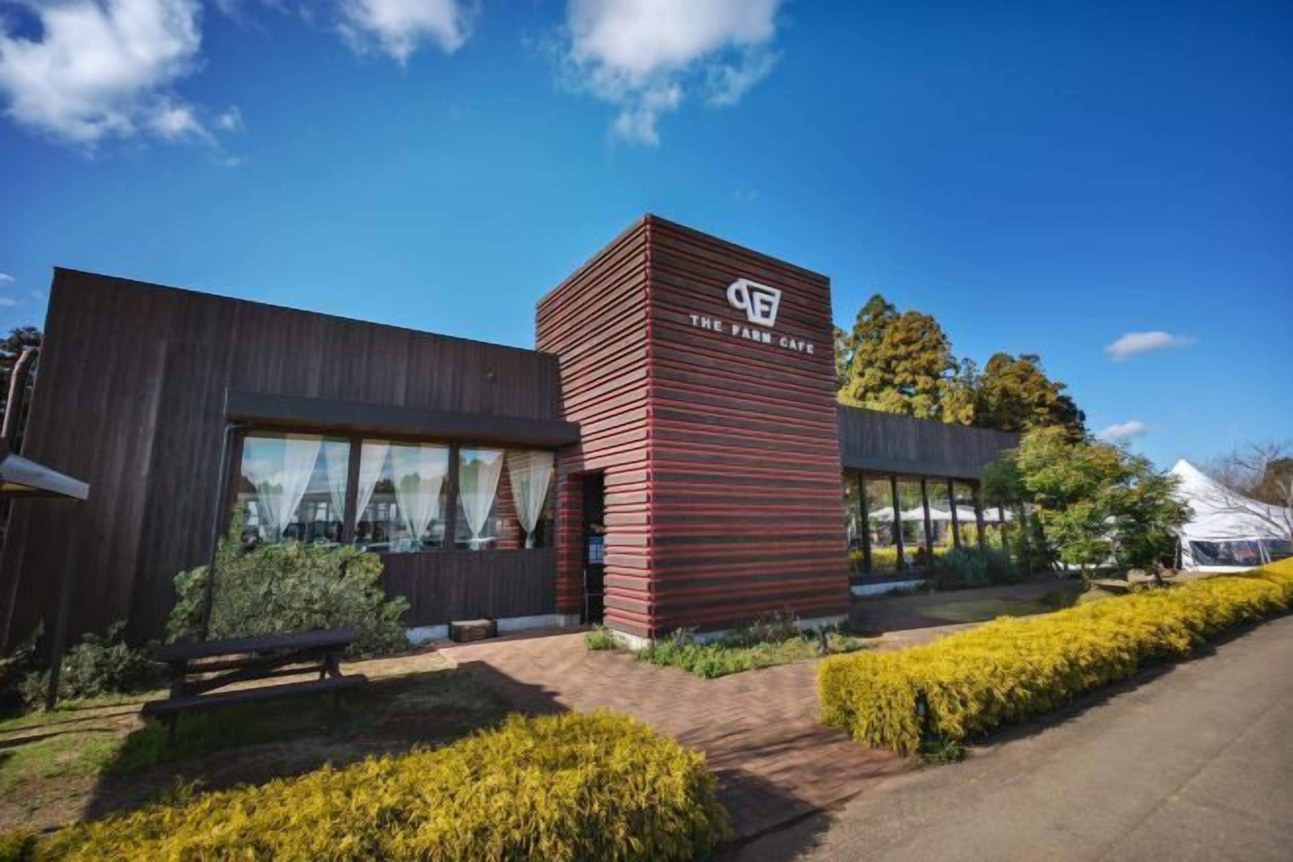 Een modern gebouw met een opvallende gevel in rood en bruin, grote ramen en een verzorgde tuin.