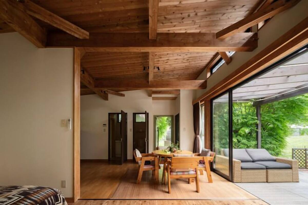 A spacious room with a wooden ceiling, a dining area with a table and chairs, and a large sliding glass door leading to an outdoor area with a sofa.