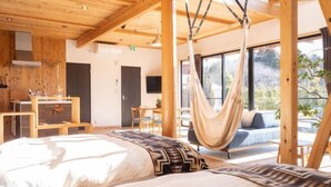 Une chambre avec un lit, un hamac, un bureau et une vue sur l’extérieur.