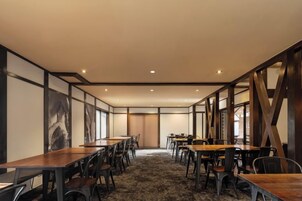 Un salón de conferencias con largas mesas y sillas, piso alfombrado y amplios ventanales.