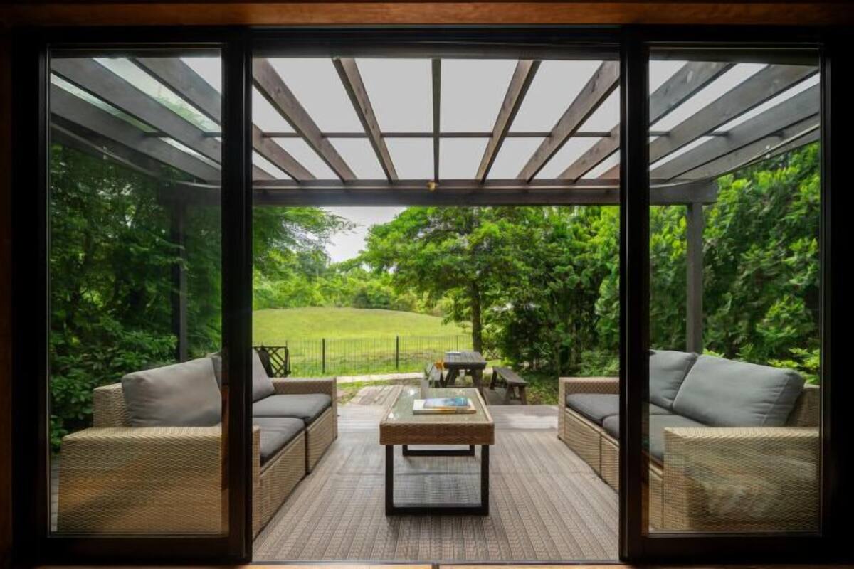 A covered patio area with wicker furniture and a central table, overlooking a lush green landscape.