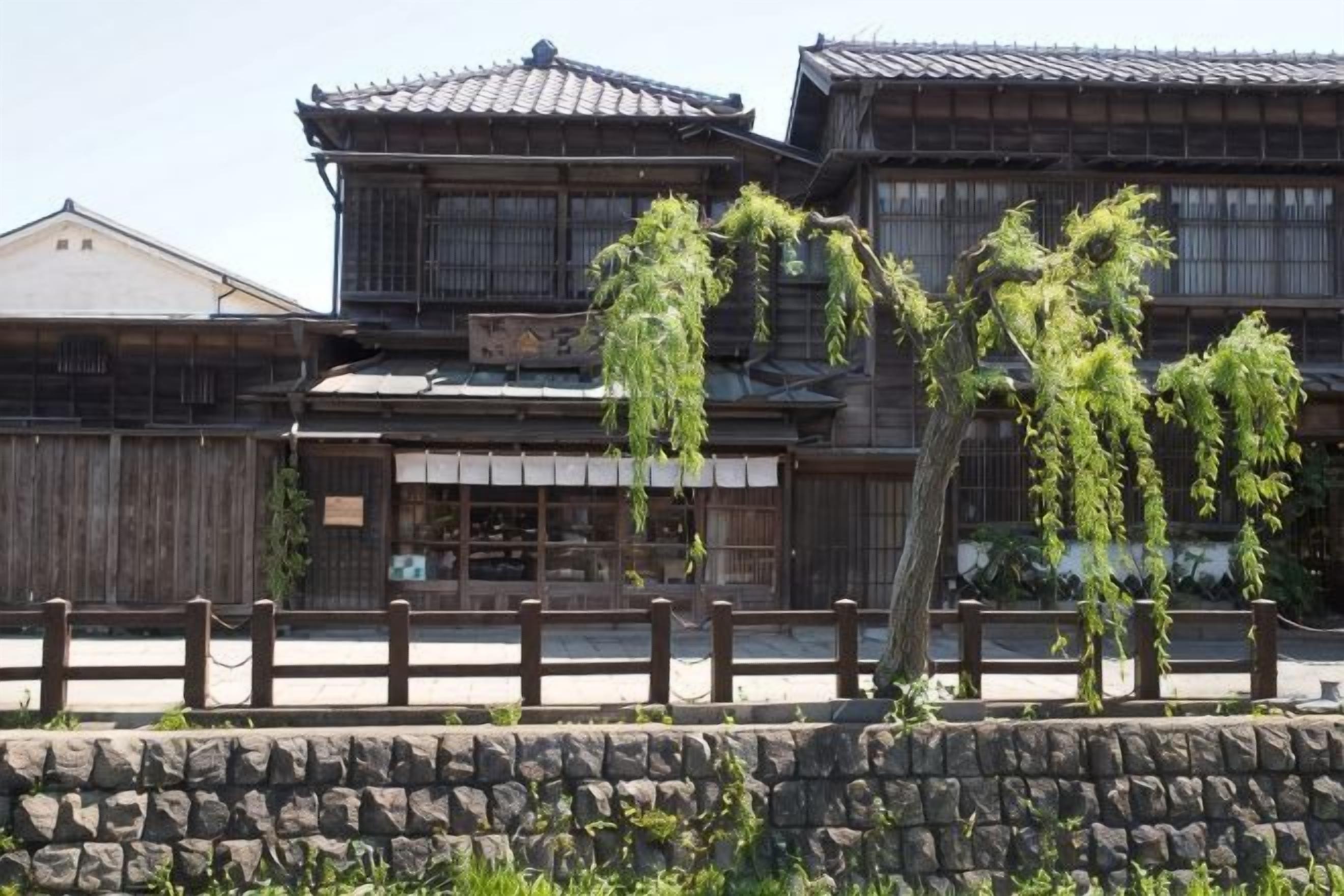 Um edifício japonês tradicional com arquitetura de madeira e um muro de pedra em primeiro plano.