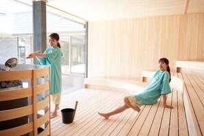 Puuinen terassi, jossa on sauna-alue, puinen penkki ja saunarakennus.